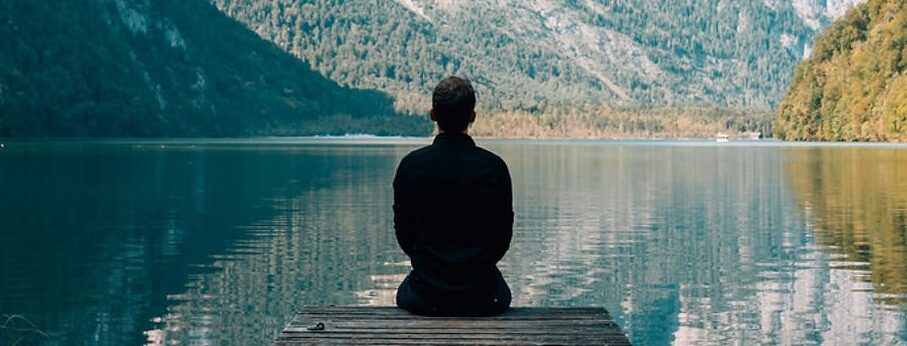 Personne assise sur un ponton qui regarde un lac et les montagnes